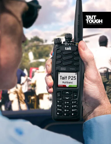 Person holding Tait TP-9900 multi-band portable radio displaying "Tait P25" on screen, showcasing its rugged design and functionality in a public safety context.